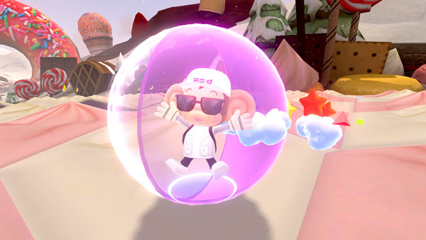 A monkey stands alone in a transparent clear and pink ball with his arms outstretched as though he is cheering. He is earing a hat and sunglasses on what appears to be a sweets-themed level.