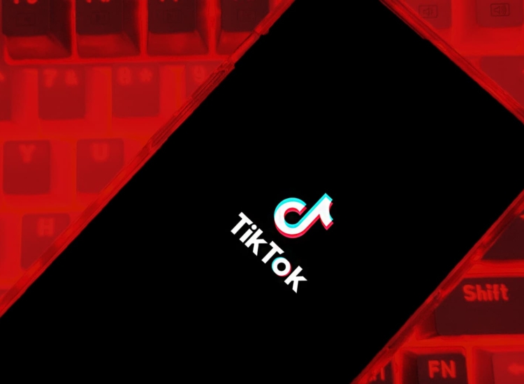 Tiktok logo on a mobile phone held over a keyboard with a red background