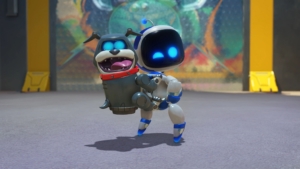 Astro Bot stands with his robot dog friend. Astro is a small robot with a white body. His arms and legs come to a rounded end, tipped in blue. his face looks like a black screen with two blue eyes, one of which is winking. The robot dog is on Astro's back, almost like a grey backpack. The robot dog seems to be smiling, with his tongue sticking out. Like Astro, the robot dog's eyes appear as blue lights on a black screen. 